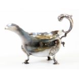 A George III silver sauce boat, with flared rim, flying acanthus scroll handle and leaf capped tripl