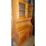 A pine kitchen cabinet with double glazed doors raised above an open shelf, the sub section with two