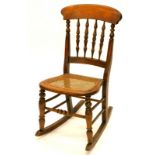 A Victorian beech rocking side chair, with a spindle turned back and a caned seat on turned legs.