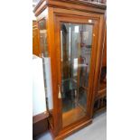 A modern cherry display cabinet, with fixed moulded top, raised above a glass panel door