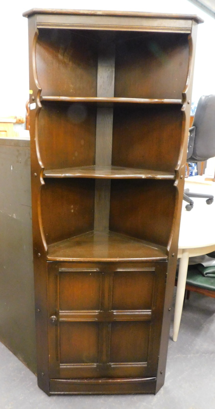 An Ercol style free standing corner cupboard, with open shelves above panelled door on a block base,