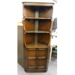 An Ercol style free standing corner cupboard, with open shelves above panelled door on a block base,