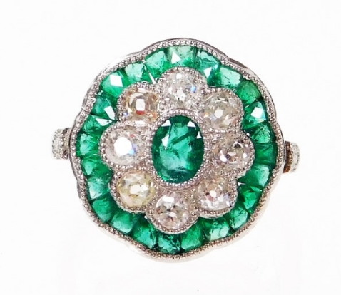 An emerald and diamond daisy style ring, the centre with oval cut emerald, surrounded by old cut dia