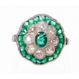 An emerald and diamond daisy style ring, the centre with oval cut emerald, surrounded by old cut dia