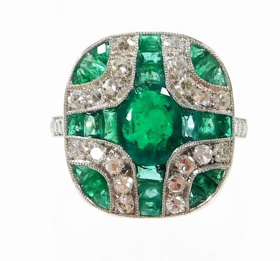 An Art Deco style emerald and diamond ring, with central oval cut emerald and further baguette cut e