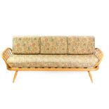 An Ercol light elm and beech three seater studio couch, with loose floral pattern cushions, raised