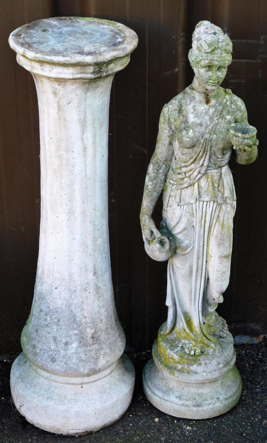 A stone garden statue of a classical lady, in flowing robes, on an inverted circular base, with a