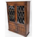 A 20thC oak glazed bookcase, with carved frieze above an astragal glazed door and a pair of linen