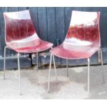 A pair of fibreglass style shaped chairs, with red textured one piece backs and seats, on a chrome