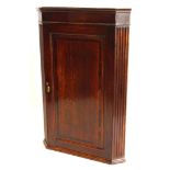 An early 19thC oak and mahogany cross banded hanging corner cabinet, with a single panelled door