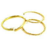 Three bangles, two yellow metal rope twist bangles, with safety clasps, and another with hammered