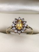 A CITRINE AND DIAMOND DAISY/CLUSTER RING the oval-shaped citrine is set within a surround of