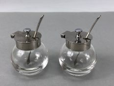 Pair of circular glass salts with silver coloured lids & Matching spoons marked "T 18 - 8"