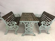 Wooden garden table and two benches with green painted cast iron ends and table base, benches approx
