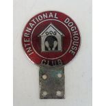 An International Doghouse Club car badge in red enamel with kennel design to the centre.