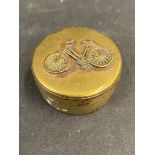 A small brass pill pot with a lady's bicycle image to the lid.