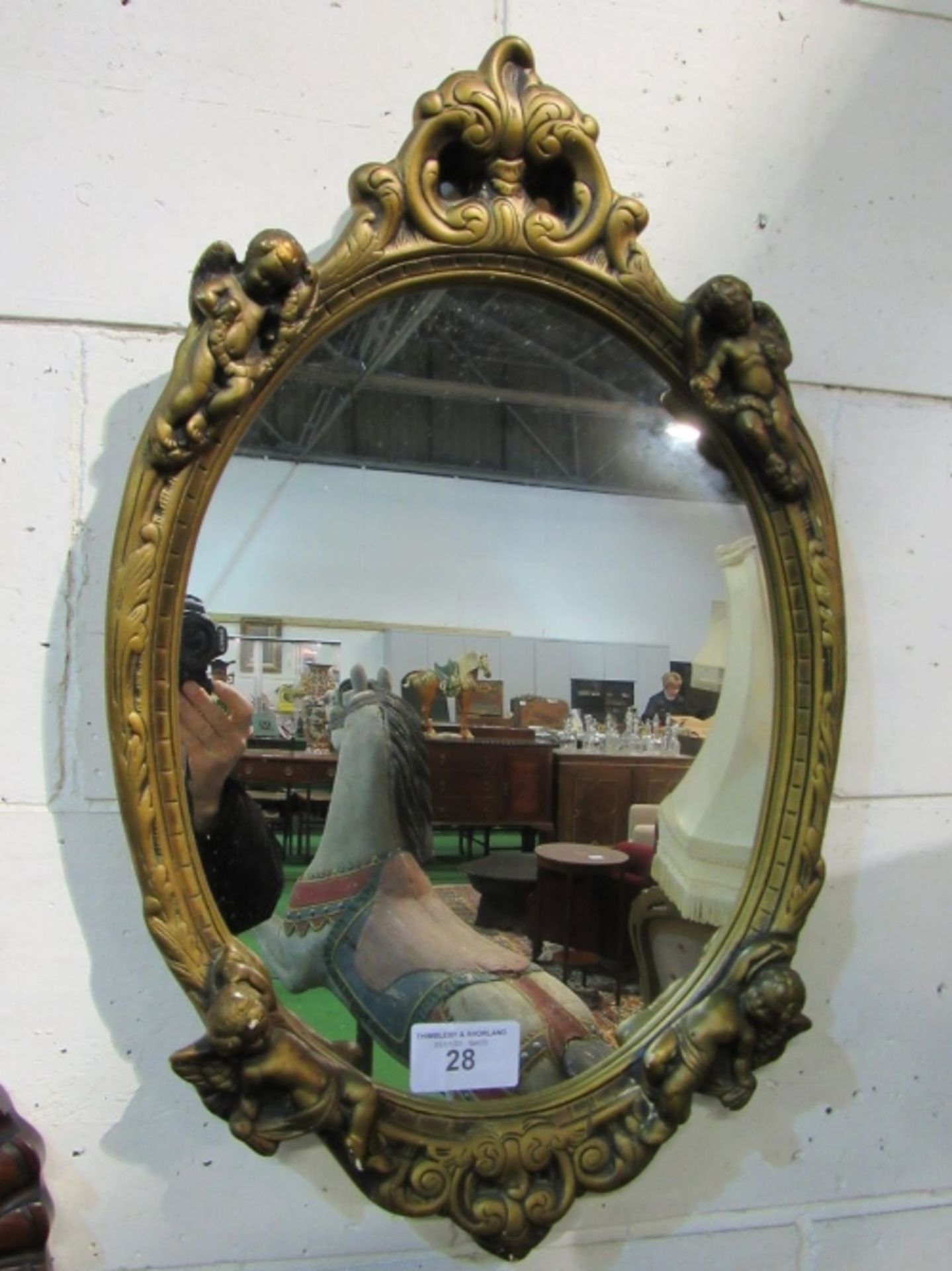 Oval wall mirror in gilt frame, decorated with putti, 69 x 44. Estimate £20-30