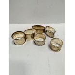 A pair of silver napkin rings and four others.