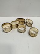 A pair of silver napkin rings and four others.