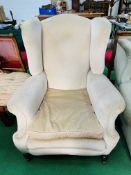 A large beige upholstered Victorian armchair on casters. 92 x 90 x 110cms.