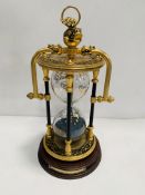 A brass decorative hourglass on wooden base.