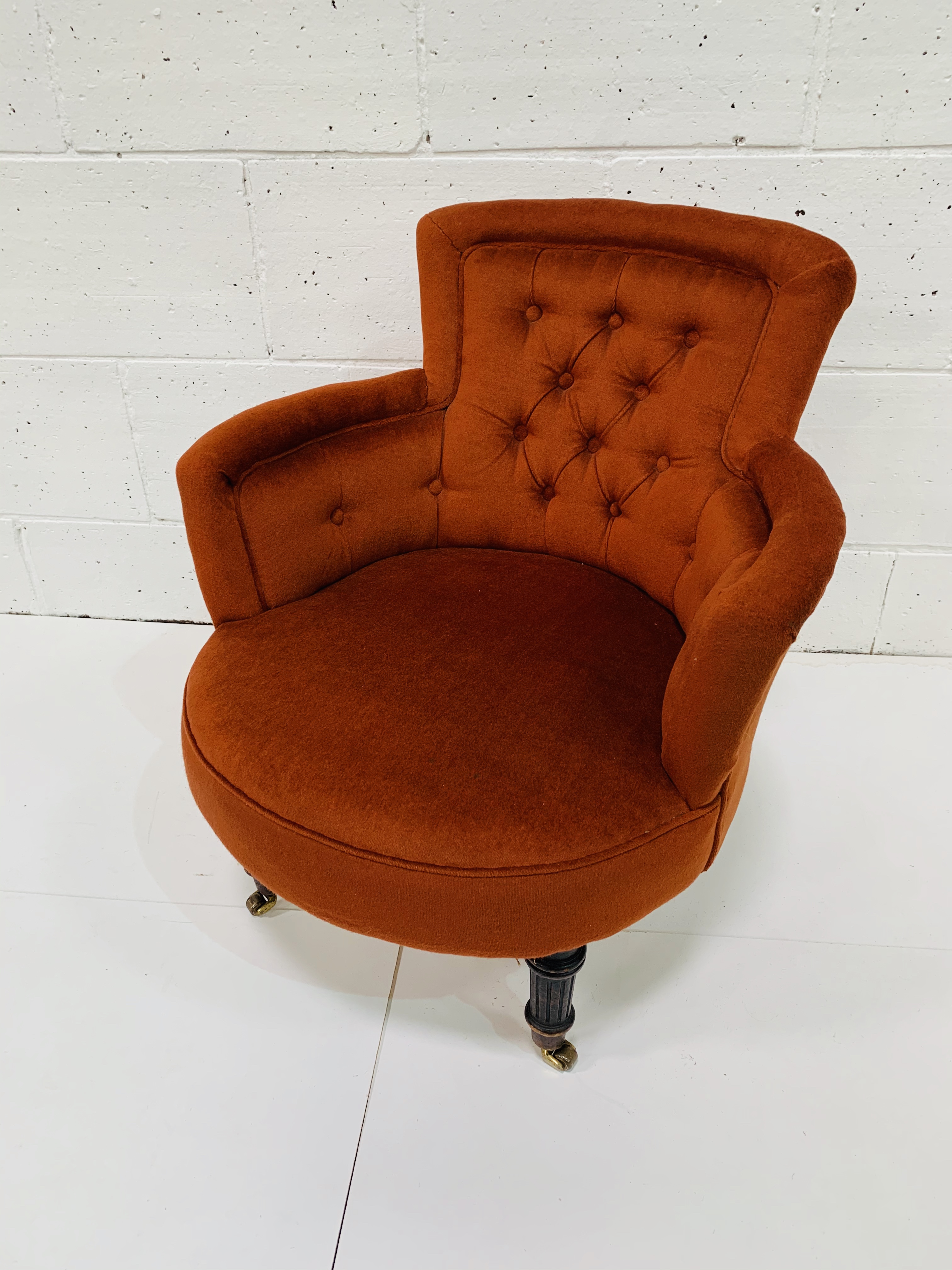Small burnt orange tub chair, on turned front legs on casters.