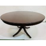 Mahogany circular tilt top table on central pedestal to four feet with casters.
