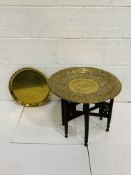 Indian brass top table on carved collapsable six legged stand, together with a brass tray.