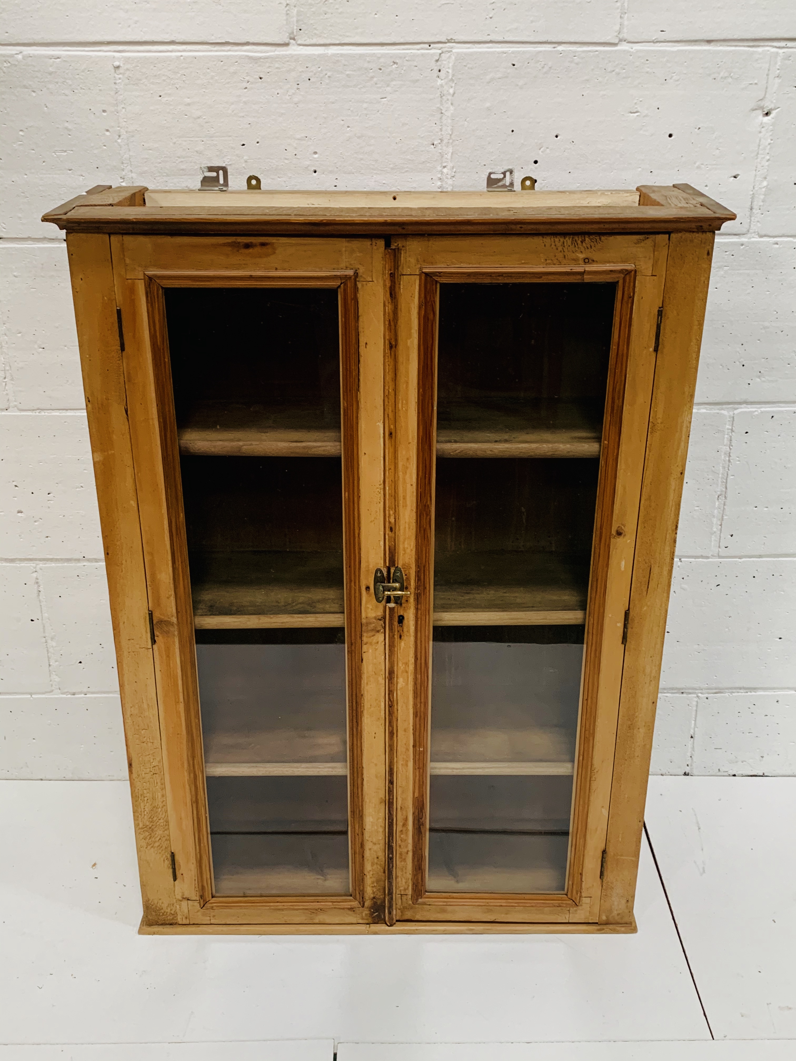 Pine wall mounted cupboard with glazed doors, 80 x 27 x 100cms.