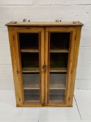 Pine wall mounted cupboard with glazed doors, 80 x 27 x 100cms.