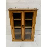 Pine wall mounted cupboard with glazed doors, 80 x 27 x 100cms.