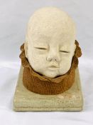 Sculpture of a baby's head emerging from a flower, on base.