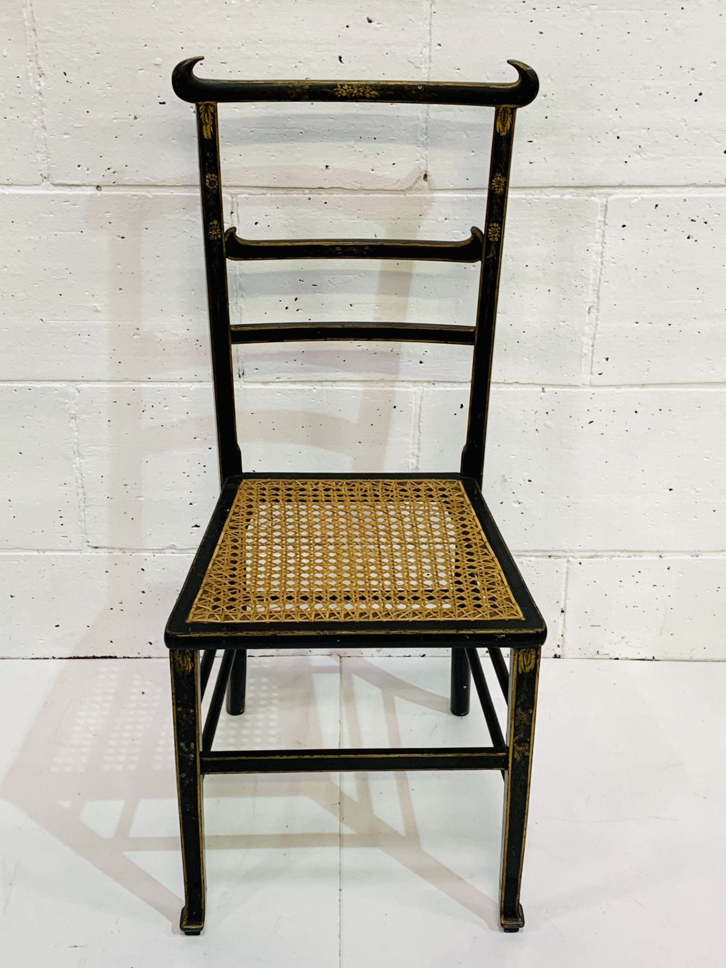 Ebonised and gilt decorated cane seat ladder back chair.