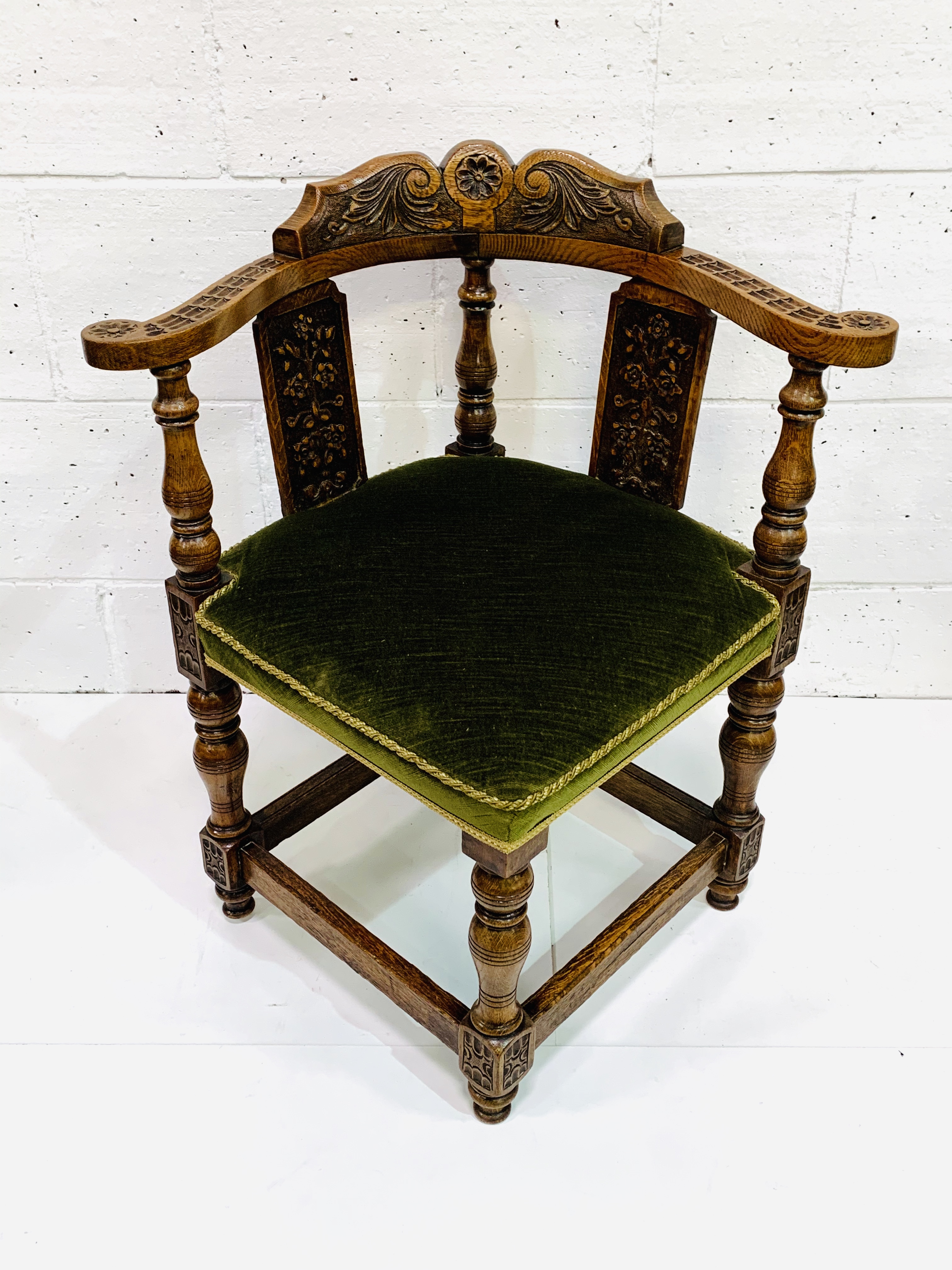 Oak framed corner chair, heavily carved, with green upholstered seat.