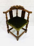 Oak framed corner chair, heavily carved, with green upholstered seat.