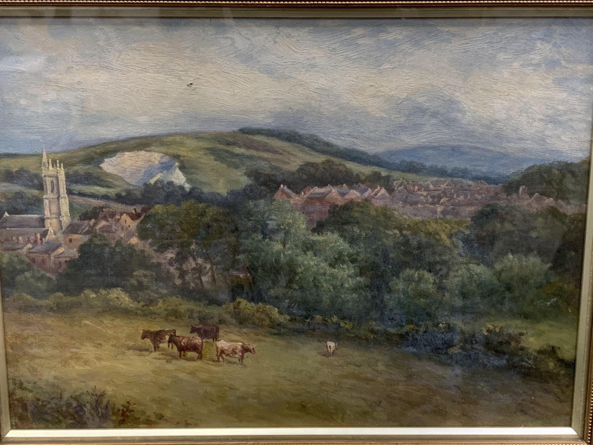 Framed and glazed oil on canvas of cows and a church in the distance.