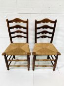 Two oak framed ladder back chairs with string seats.