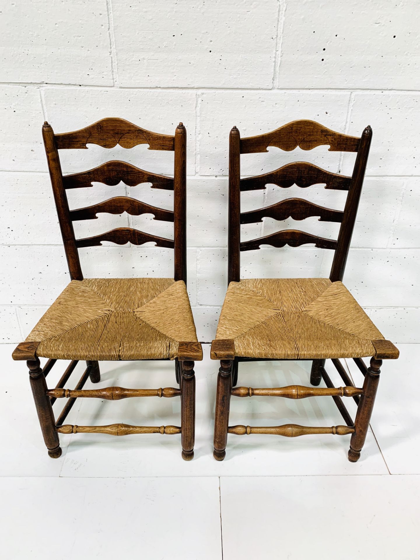 Two oak framed ladder back chairs with string seats.