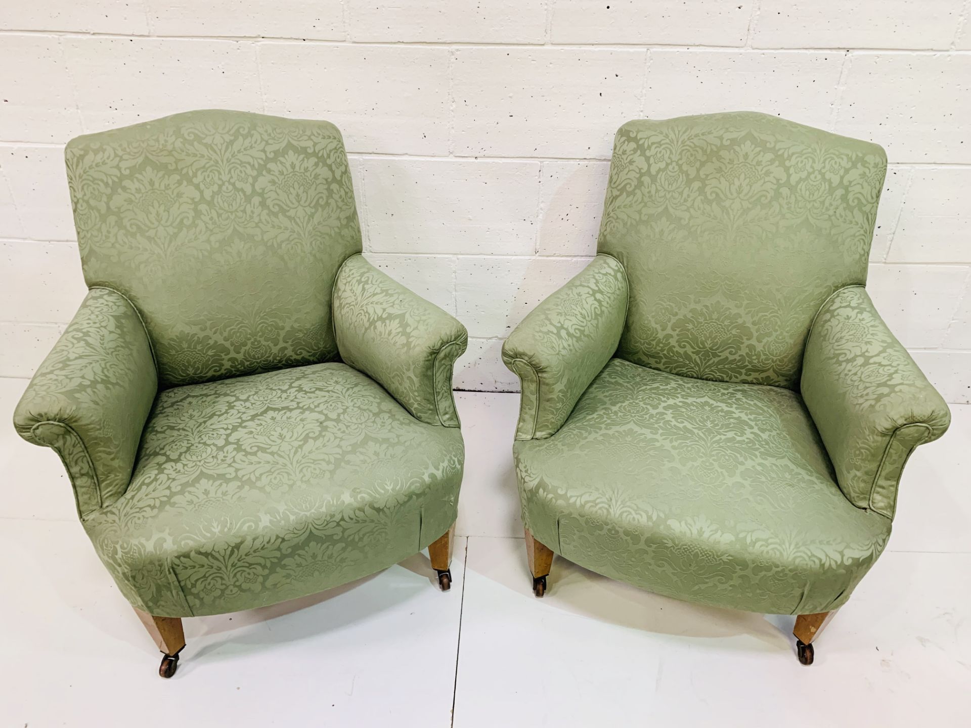 Pair of green upholstered arm chairs on ceramic casters.