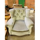 A large green upholstered Victorian armchair on casters.