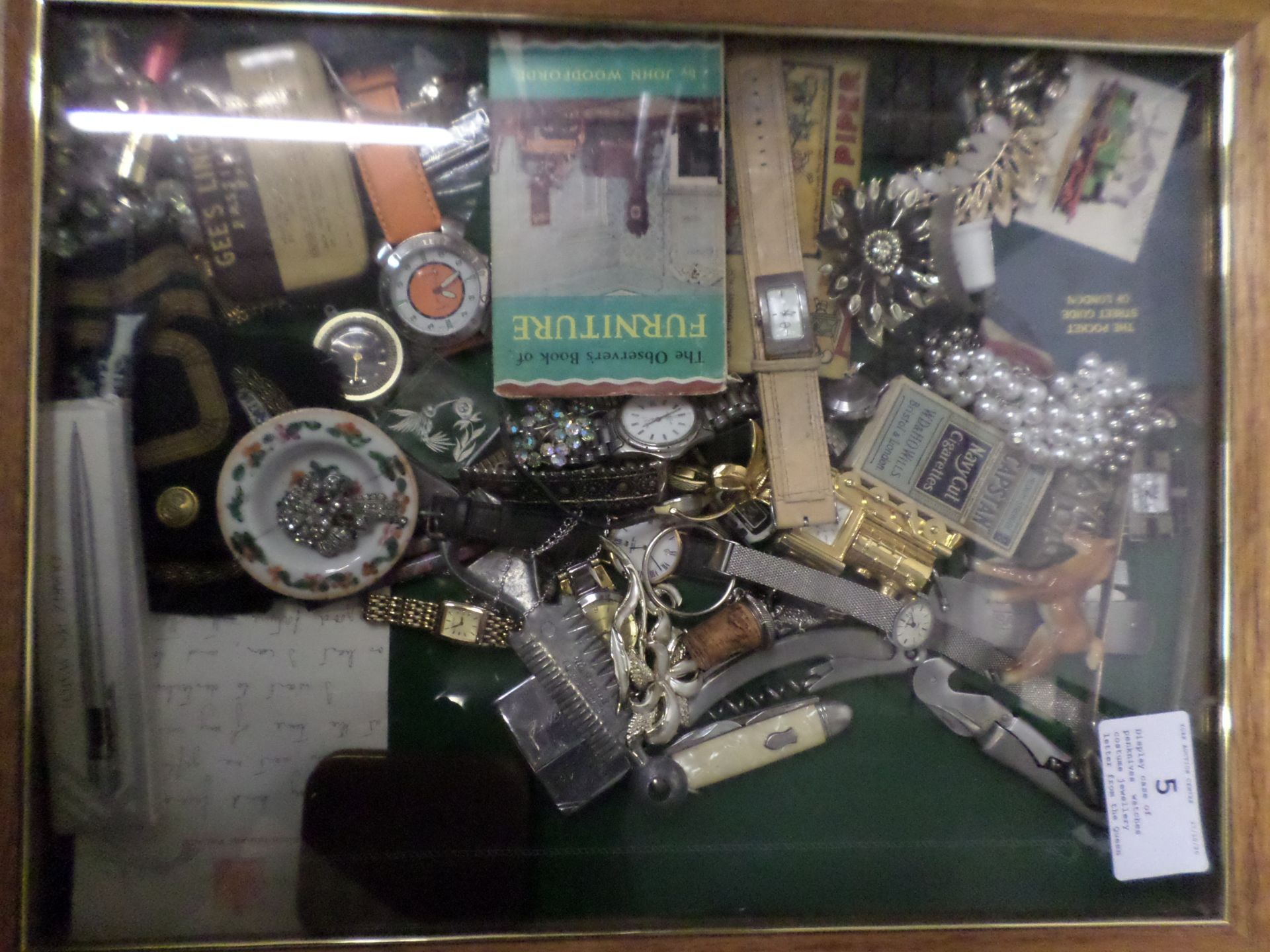 Display case of penknives, watches, costume jewellery, letter from the Queen