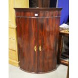 A mahogany bow front corner cupboard.