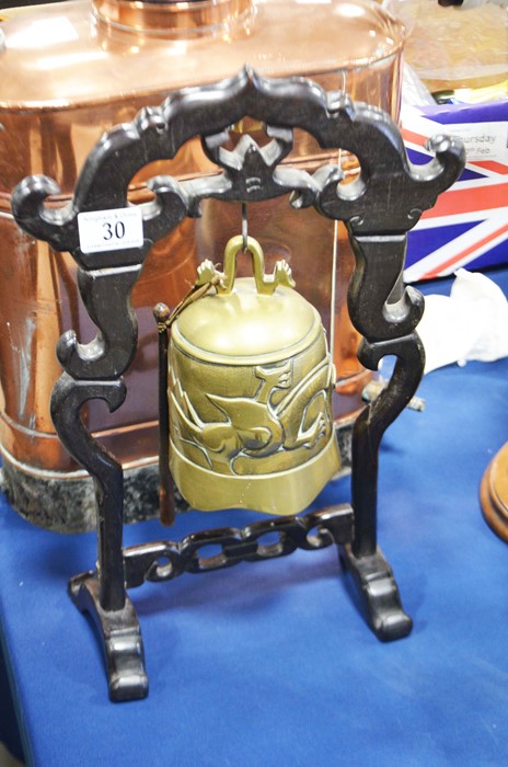 A brass temple bell on pierced wooden stand.