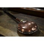 A copper warming pan with turned ebonised handle.
