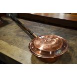 A copper warming pan with turned ebonised handle.