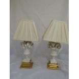A pair of Belleek style lamps with central ceramic campana urn with fruit and foliage, raised on