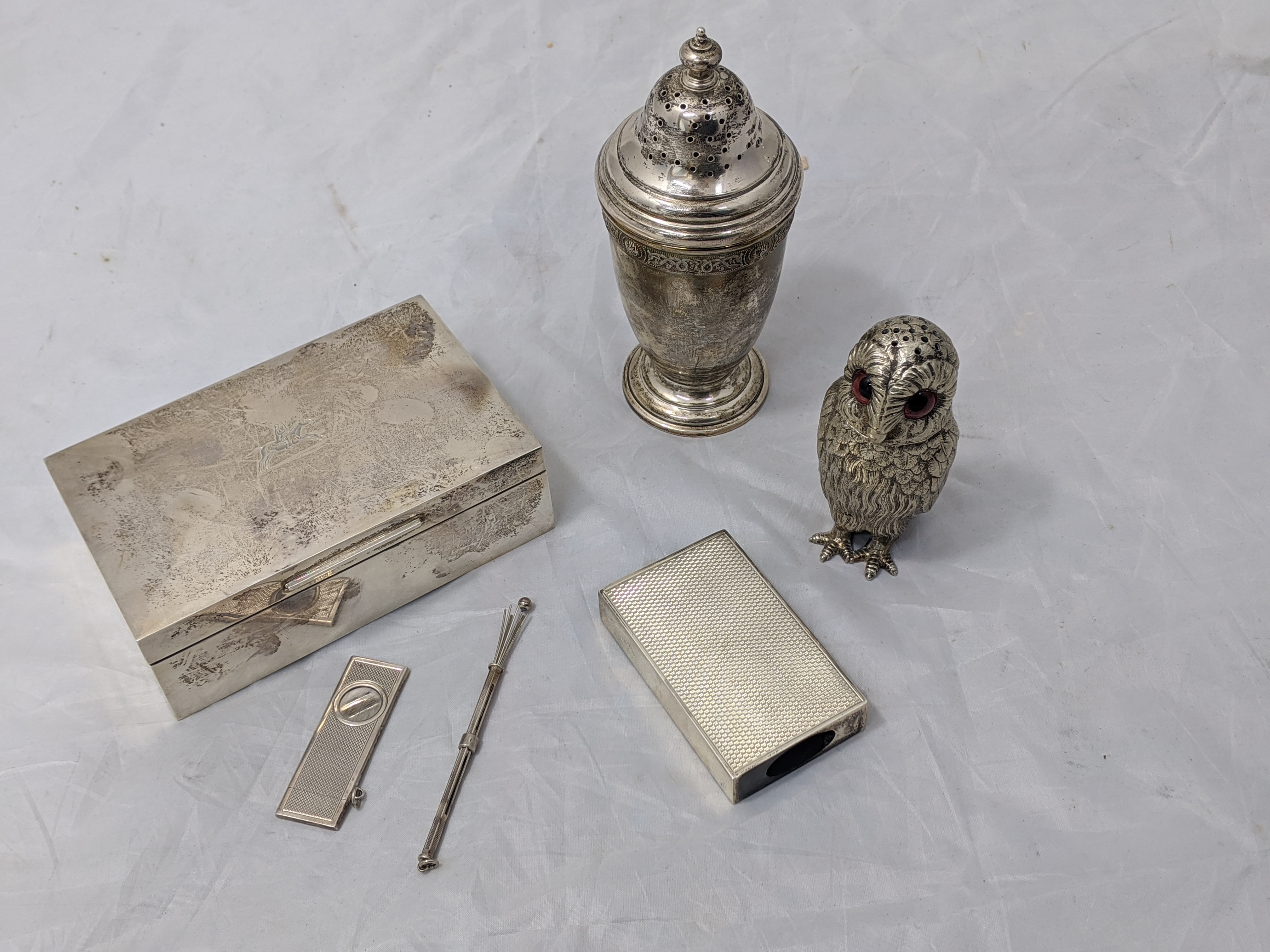 A silver box with horserider crest, a silver pepperette, a silver match box case, a silver twizzle