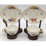 A pair of Meissen cups and saucers on wooden stands, marks to base, saucer W.14cm