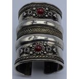 A Middle Eastern or Indian white metal tribal bangle, mounted with two red stones, 69g, L.7.5cm