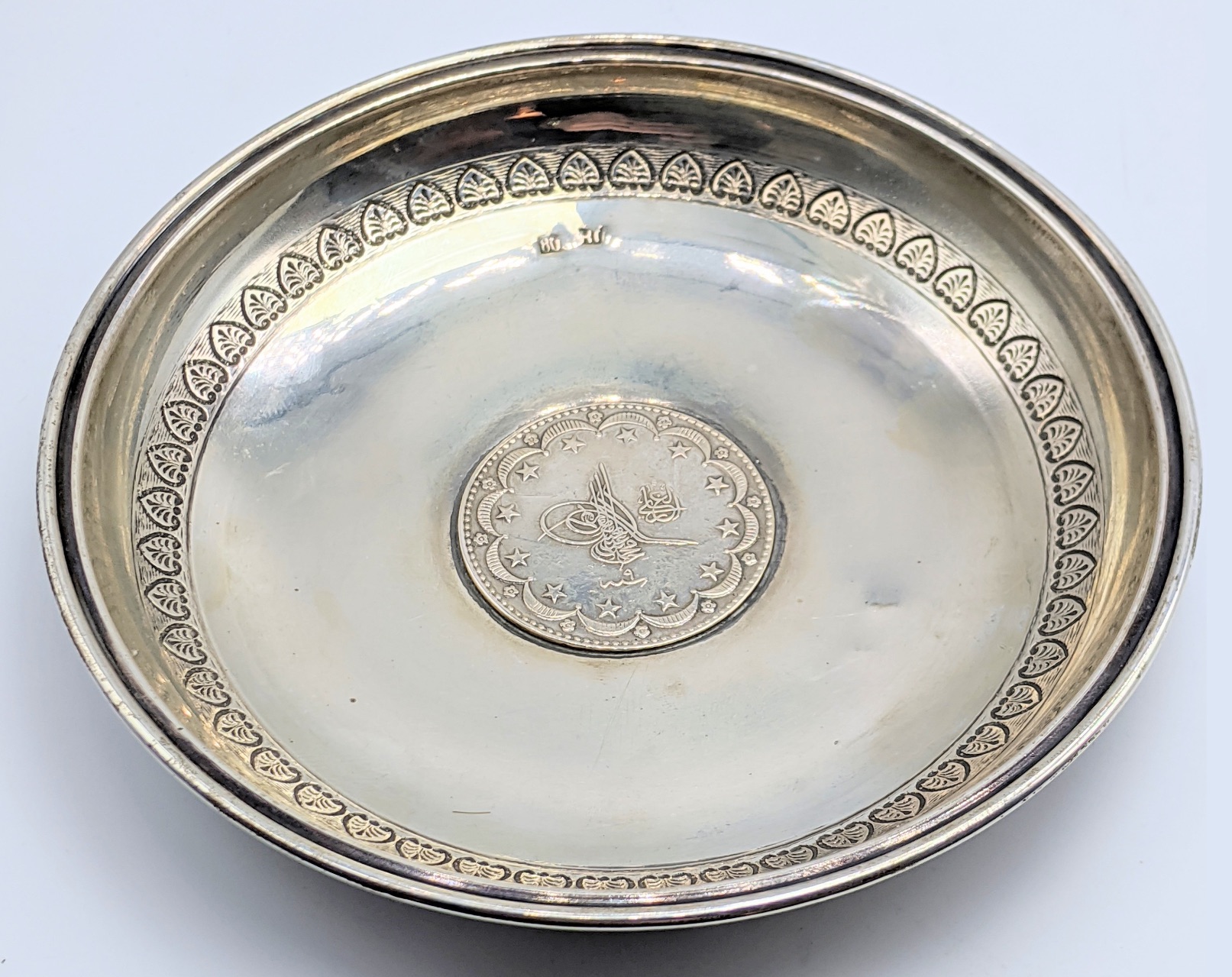 A Turkish silver dish with central silver coin, marked to inside, etched outer band, 64g, D.13cm